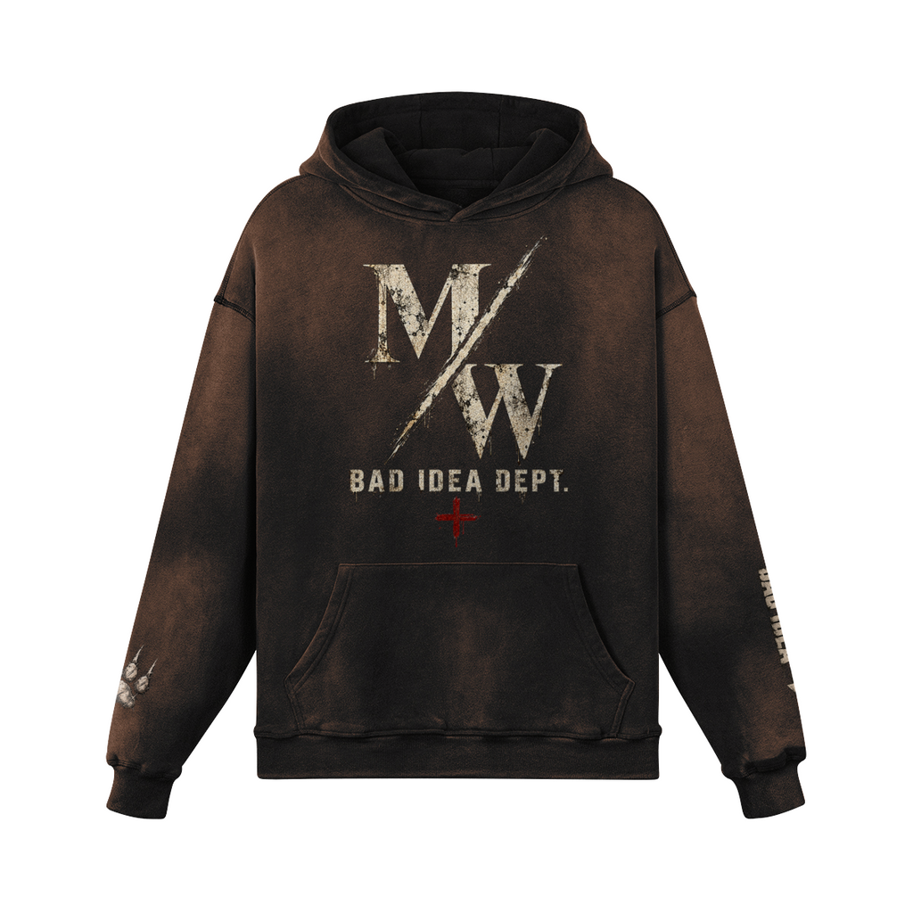 A dark brown acid-wash pullover hoodie featuring a distressed white 'M/W' logo and 'BAD IDEA DEPT.' text on the front, with a small red cross accent below and additional graphics on the sleeves, shown against a plain white background.