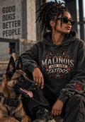 A woman wearing a dark gray graphic hoodie and sunglasses sits with a German Shepherd dog. The hoodie features a graphic print that reads 'MALINOIS ARE LIKE TATTOOS' with a dog illustration and paw print.