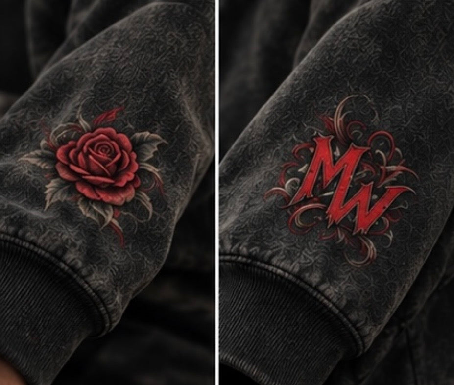 Close-up of a black distressed bomber jacket sleeve showing two custom designs: a red rose with gray leaves on the left cuff and a red stylized 'MW' monogram with gray scrollwork on the right cuff.